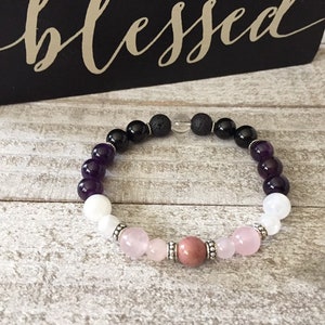 May include: A multi-colored beaded bracelet with amethyst, white, rose quartz, and pink beads. The bracelet also includes black lava beads and silver spacers.