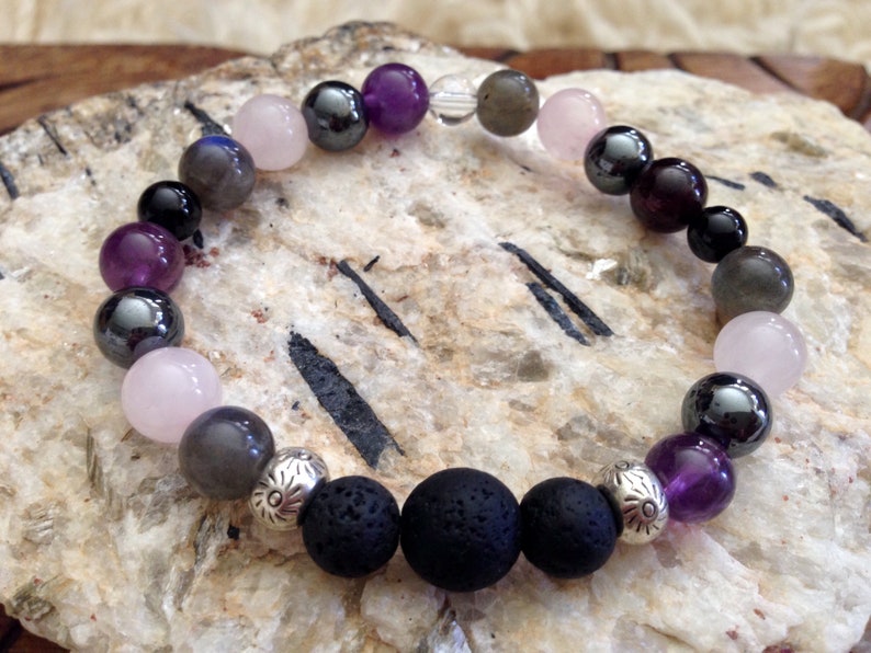May include: A beaded bracelet featuring amethyst, rose quartz, hematite, labradorite, and lava rock beads. The bracelet has silver spacers with floral designs.