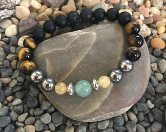 May include: A beaded bracelet with black, brown, yellow, and green stones. The bracelet has a lava rock bead and silver beads.