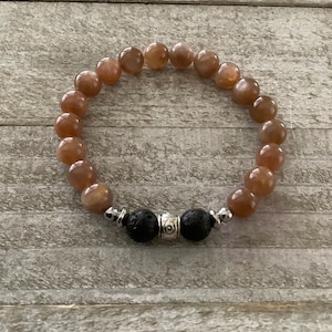 May include: A brown sunstone beaded bracelet with black lava beads and a silver charm.