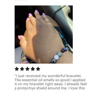 May include: A close-up of a person's wrist wearing a beaded bracelet with purple, black, grey, and white stones. The bracelet is described as an "Empath Protection Bracelet" and is said to provide a "protective shield".