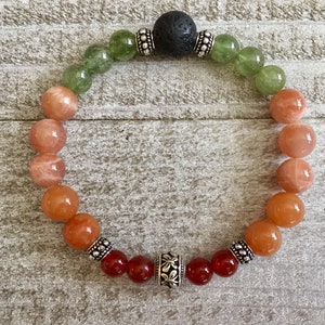 May include: A multi-colored gemstone bracelet with silver beads and a black lava bead. The bracelet features green, orange, and red gemstones.