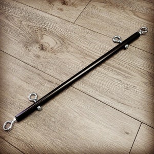 May include: A black metal bar with silver rings on each end. The bar is lying on a wooden surface.