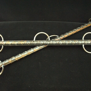 May include: Two silver metal bars with a textured surface and three circular rings on each bar. The bars are crossed over each other.