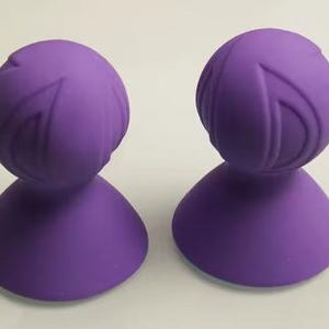 Peut inclure: Deux ventouses en silicone violet avec un dessus arrondi texturé et une base plate.