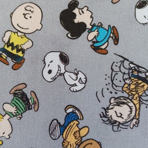 May include: A gray fabric with a repeating pattern of Peanuts characters, including Snoopy, Charlie Brown, Lucy, and Woodstock. The characters are depicted in various poses, such as walking, running, and playing.