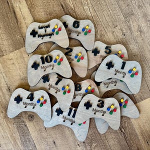 May include: A set of ten wooden game controllers with colorful dots and black numbers. Each controller has a different number of months written on it, from 1 to 11. The controllers are made of light brown wood and have a rustic look.