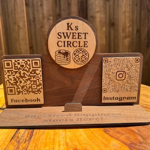 May include: Wooden business card holder with the text "Ks Sweet Circle" and QR codes for Facebook and Instagram. The holder features a circular emblem with pancakes and waffles.