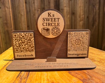 Op de afbeelding: Houten visitekaarthouder met de tekst "Ks Sweet Circle" en QR-codes voor Facebook en Instagram. De houder heeft een cirkelvormig embleem met pannenkoeken en wafels.