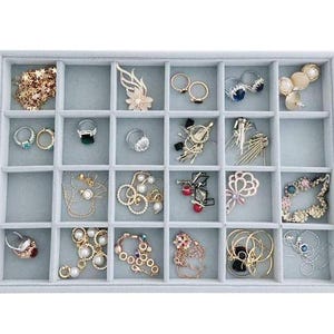 May include: A gray velvet jewelry tray with 18 compartments for storing rings, earrings, necklaces, and other small jewelry items.