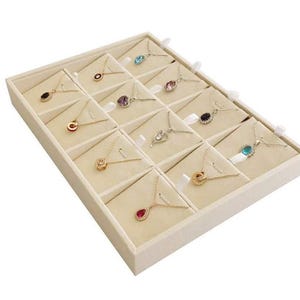 May include: A display tray filled with various necklaces. Each necklace features a delicate chain and a pendant in different shapes and colors, including red, blue, and purple. The tray is beige and has individual compartments for each necklace.