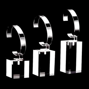 May include: Three clear acrylic watch display stands of different sizes. Each stand features a curved arm to hold a watch securely.