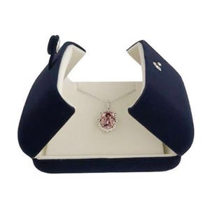May include: A navy blue velvet jewelry box with a white interior, open to reveal a silver necklace with a pink gemstone pendant.