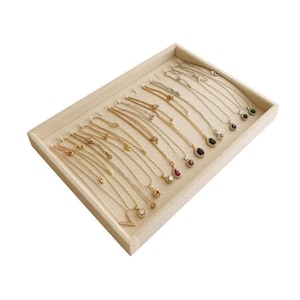 May include: A display tray filled with various necklaces. The necklaces feature gold and silver chains with pendants of different shapes and colors, including red, black, and green gemstones. The tray is beige and has individual slots for each necklace.