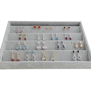 May include: A gray velvet earring display tray filled with various pairs of earrings. The earrings include studs, dangles, and drop styles in silver, gold, and gemstone accents. The tray is tiered for easy viewing.