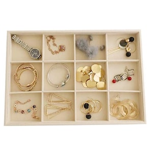 May include: A beige jewelry organizer filled with various accessories. Items include a silver watch, gold necklaces, bracelets, earrings, and a fluffy gray accessory. The organizer is divided into multiple compartments.
