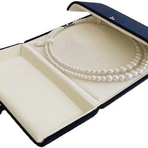 May include: A navy blue velvet jewelry box with a white interior. The box is open and a pearl necklace is inside.