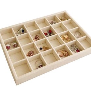 May include: A beige velvet jewelry tray with 24 compartments for storing rings, earrings, and other small jewelry items.