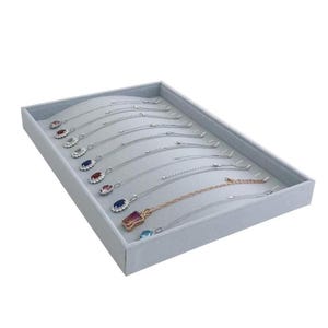May include: A gray jewelry display tray filled with various necklaces. The necklaces have silver chains and colorful gemstone pendants. The tray is rectangular and has a soft, padded interior to protect the jewelry.