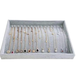 May include: A gray velvet jewelry display tray filled with various gold and silver necklaces. The necklaces have different pendant designs, including gemstones and simple shapes. The tray is rectangular and has individual slots for each necklace.