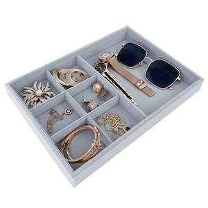 May include: A white jewelry organizer with a gray velvet lining, holding various accessories. Items include a gold watch, sunglasses, rings, earrings, a bracelet, and necklaces. The organizer is divided into multiple compartments.