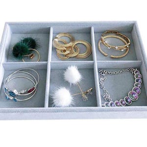 May include: A light gray velvet jewelry tray with six compartments, filled with various jewelry pieces. Includes gold bracelets, a silver necklace with iridescent stones, and earrings with green and white accents.
