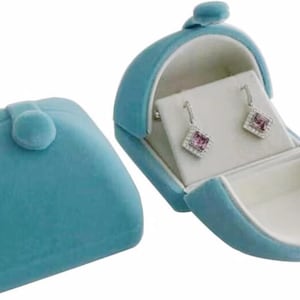 May include: A light blue velvet jewelry box with a hinged lid. The box is open and shows a pair of silver earrings with pink stones.