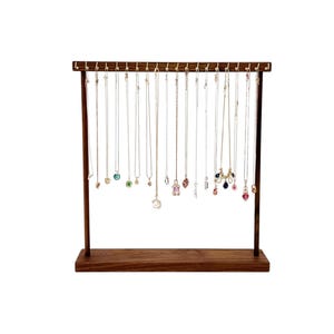 May include: A wooden jewelry stand with 20 hooks for hanging necklaces. The stand has a dark brown finish and a rectangular base. The necklaces are made of gold and silver chains with various colored gemstones.