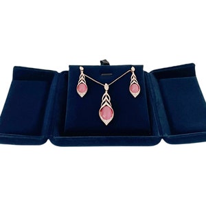 May include: A rose gold necklace and earrings set with pink stones and clear crystal accents. The jewelry is displayed in a blue velvet box.