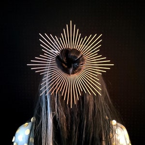 Könnte beinhalten: Ein goldfarbener Haarkamm mit einem Sternburst-Design. Der Kamm wird im Haar einer Person getragen.