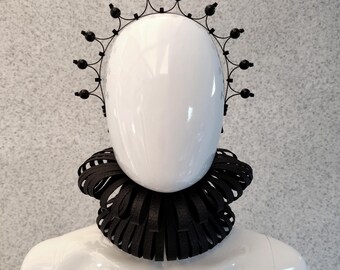 Può includere: Una corona in metallo nero con accenti rotondi si trova sulla testa di un manichino bianco. Un colletto in tessuto nero con un design a balze è indossato attorno al collo del manichino. Il testo "Ziptie Jewelry" è visibile nella parte inferiore dell'immagine.