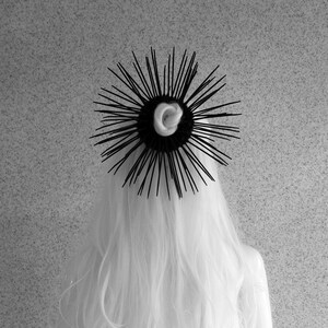 May include: Black hair comb with a spiky design. The comb is made of black plastic and has a circular shape. The comb is worn in a person's hair.