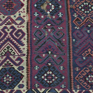 May include: A woven textile featuring vertical panels with geometric patterns in shades of deep blue, magenta, and cream. The design includes repeating diamond and angular motifs with visible signs of wear and fraying along the central section.