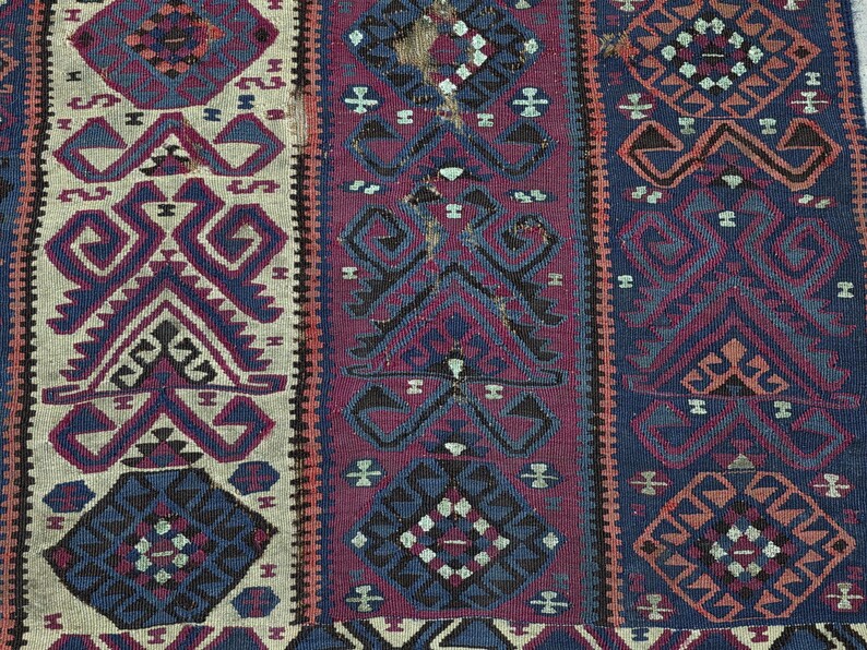 May include: A woven textile featuring vertical panels with geometric patterns in shades of deep blue, magenta, and cream. The design includes repeating diamond and angular motifs with visible signs of wear and fraying along the central section.