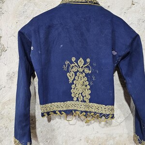K&ouml;nnte beinhalten: Eine marineblaue Vintage-Jacke mit goldener Stickerei. Die Jacke hat aufwendige goldene Blumenstickereien auf dem R&uuml;cken und an den Kanten. Lange &Auml;rmel und ein robuster Stoff sind sichtbar. Historisches Kleidungsst&uuml;ck.