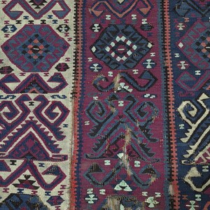 May include: A woven textile featuring vertical panels in cream, deep magenta, and navy blue. The fabric displays repeating geometric patterns, including stylized diamonds and angular motifs in contrasting colors, with visible signs of wear.