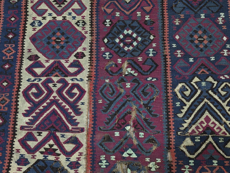 May include: A woven textile featuring vertical panels in cream, deep magenta, and navy blue. The fabric displays repeating geometric patterns, including stylized diamonds and angular motifs in contrasting colors, with visible signs of wear.