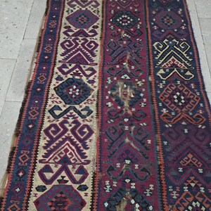May include: A rectangular woven rug featuring vertical panels with intricate geometric patterns in shades of deep red, navy blue, cream, and dark purple. The textile displays repeating diamond and angular motifs throughout the entire surface area.