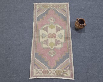 May include: A rectangular area rug featuring a central geometric medallion in shades of dusty pink, muted blue, and cream, with floral motifs at the ends and a fringed edge, accompanied by a small brown ceramic pitcher with a handle and decorative dots.