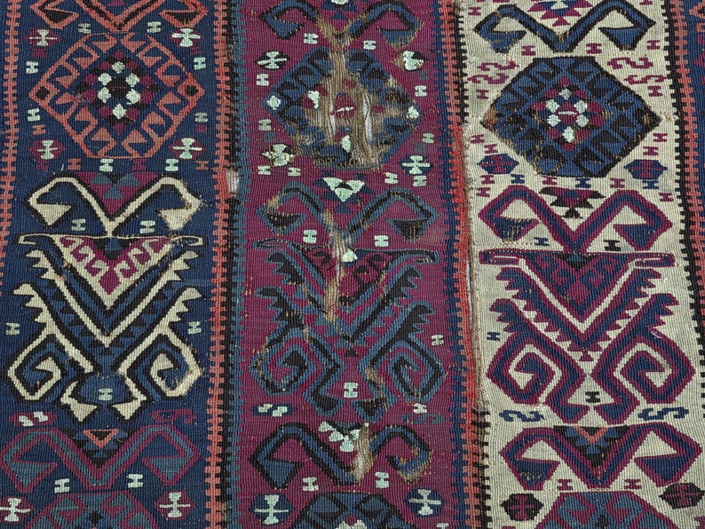 May include: A woven textile featuring vertical panels with repeating geometric patterns in shades of deep blue, magenta, and cream. The design includes stylized diamond shapes and symmetrical motifs arranged in a dense, intricate, and textured weave.