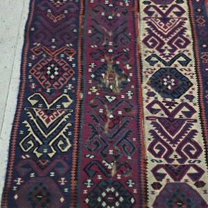 May include: A rectangular woven textile runner featuring three vertical panels with intricate geometric patterns in shades of deep blue, dark red, and cream. The design includes repeating diamond and hooked motifs with visible frayed edges.