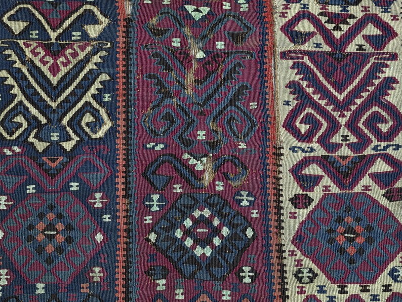 May include: A woven textile featuring three vertical panels with geometric patterns. The left panel is dark blue, the center is deep magenta, and the right is off-white. Each section displays repeating angular motifs and octagonal shapes.