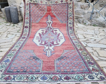 Puede incluir: Una alfombra turca vintage con fondo rojo y un medallón central de color crema. La alfombra tiene un borde floral con acentos verdes, azules y rosas.