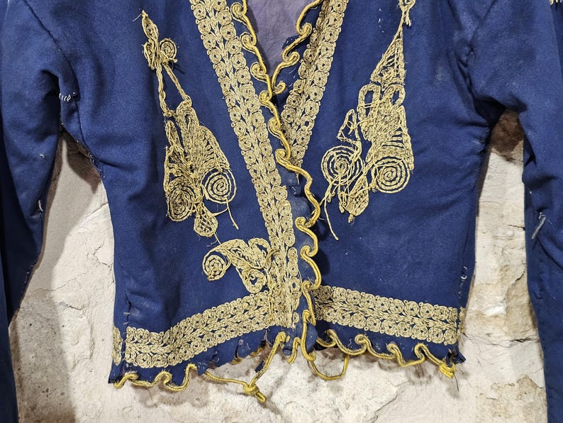 K&ouml;nnte beinhalten: Dunkelblaue Jacke mit goldener Stickerei. Die Jacke hat aufwendige Goldfaden-Designs entlang der Kanten, des Halsausschnitts und der Frontplatten. Die Stickerei umfasst Blumen- und Scrollmuster. Die Jacke hat lange &Auml;rmel und einen V-Ausschnitt.