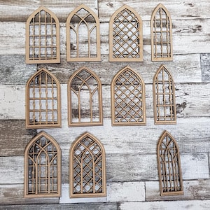 Puede incluir: Una colección de marcos de ventanas de madera cortados con láser en varios diseños de arcos góticos. Los marcos, con intrincados patrones de celosía y rejilla, están dispuestos sobre un fondo de madera envejecida.