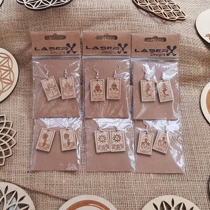 May include: Six pairs of wooden earrings with various designs, including a flower, a sun, and a person meditating. The earrings are packaged in clear plastic bags with brown cardstock backing that reads "LASERX Designs".
