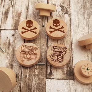 May include: Eight wooden knobs with different designs. Four knobs feature a skull and crossbones design, and four knobs feature a treasure chest design.