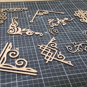 May include: A set of ten decorative wooden corner pieces with intricate designs. The pieces are made of light brown wood and have a variety of patterns, including swirls, leaves, and geometric shapes.