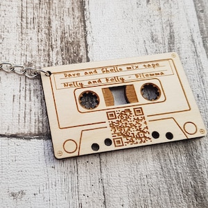 Puede incluir: Un llavero de madera con forma de cinta de casete con un código QR y el texto "Dave and Sheila mix tape Nelly and Folly - Dilemma".
