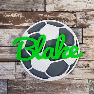 May include: A white and gray soccer ball with the name "Blake" in green letters on top.